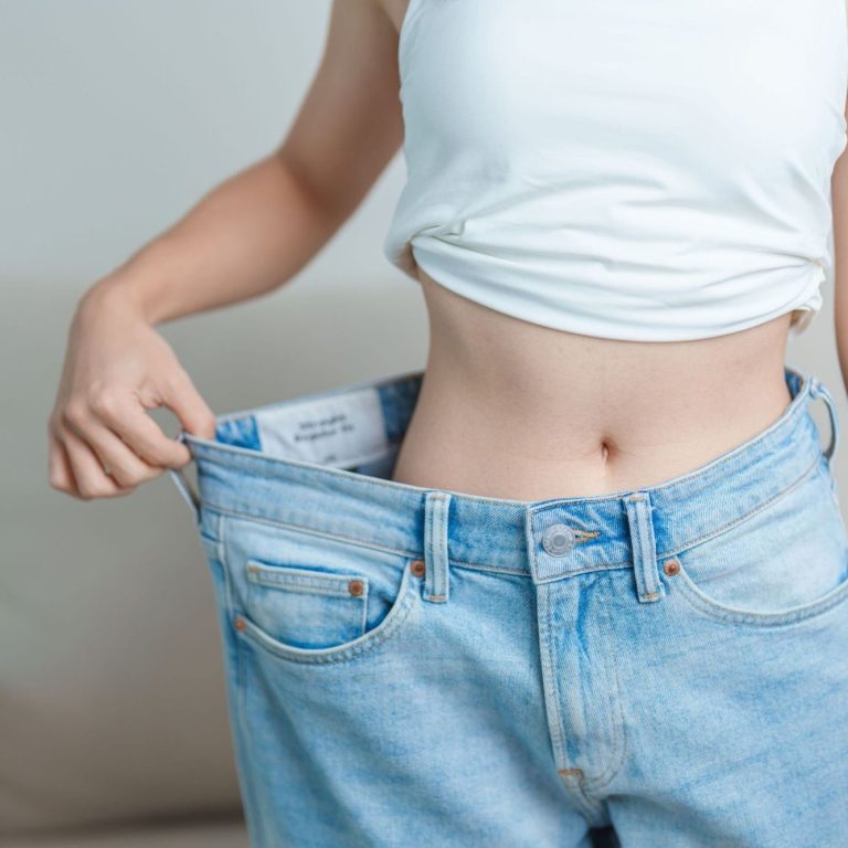 Nachhaltig abnehmen mit Fasten Junge Frau zeigt, wie weit ihre Jeans sitzt, mit lockerer Passform an der Taille.